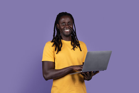 Positive black man using laptop on purple