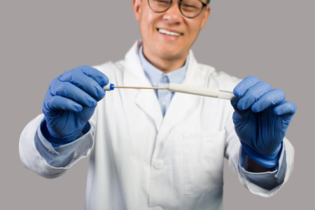 Cheerful mature chinese male therapist in white coat, glasses and protective gloves shows test for covid-19 virusの写真素材