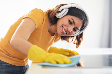 Cheerful Young Arab Woman Listening Music While Cleaning Kitchen Counterの写真素材