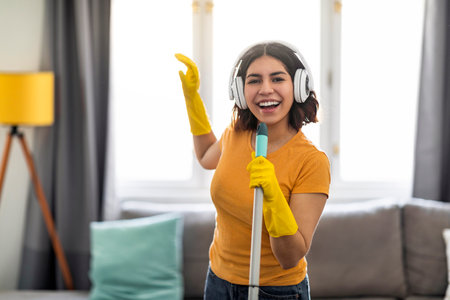 Cheerful Arab Female In Wireless Headphones Singing While Making Cleaning At Homeの写真素材