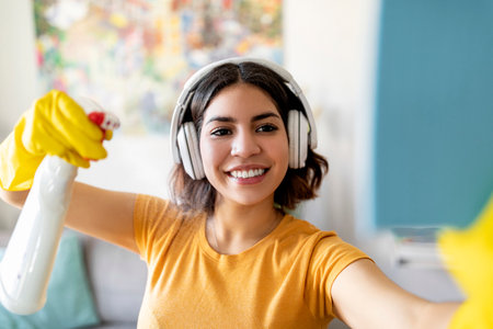 Closeup Shot Of Cheerful Arab Female In Wireless Headphones Cleaning At Homeの写真素材