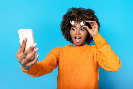 Shocked african american woman looking at phone and removing glassesの写真素材