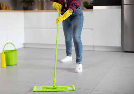Millennial african american lady in rubber gloves with bucket and mop washes floor, enjoys household...