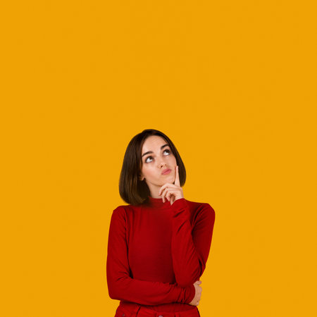 Curious pensive young woman looking at copy space on orange