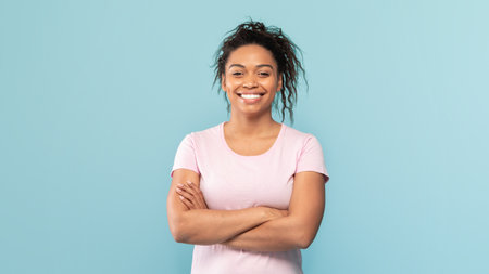 Portrait of happy african american woman standing with folded arms, looking and smiling at camera,...