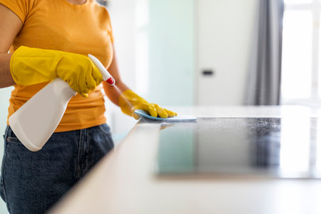 Young Woman Using Detergent Spray And Rag While Wiping Table In Kicthen