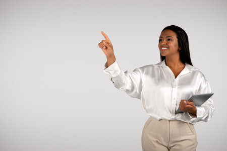 Happy young african american business woman with tablet points finger to empty space, controls virtual whiteboardの写真素材