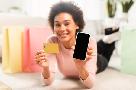 App for online shopping at home. Glad young mixed race lady shopaholic shows phone and credit cardの写真素材