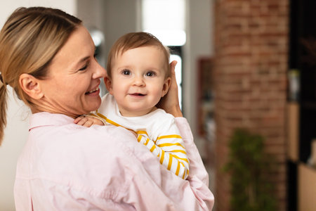 Maternal love. Mother holding cute infant girl on hands and cudding, embracing baby and smiling,...