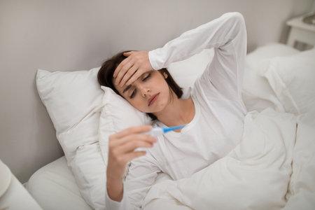 Sick woman with fever checking her temperature in bed