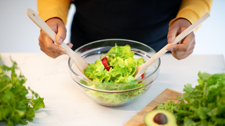 Young african american lady in apron prepare salad at table with organic vegetables in kitchen interior, top viewの写真素材