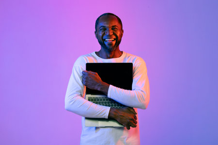 Emotional black man embracing laptop, neon light backgroundの写真素材