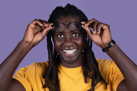 Happy millennial african american man removing eyeglasses on purple, closeup