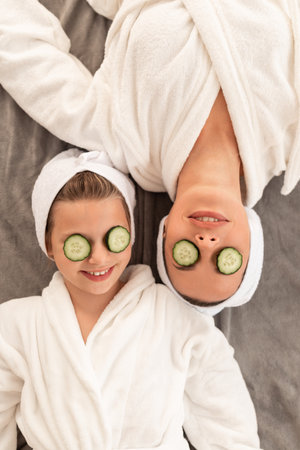 Little Girl And Mother Wearing Bathrobes Lying With Cucumber Slices On Eyesの写真素材