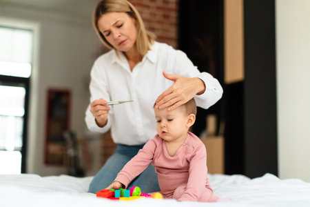 Caring mother checking temperature to her sick little baby, looking at thermometer and touching kids foreheadの写真素材