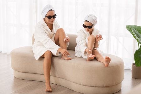 Mother and little daughter in bathrobes and sunglasses making pedicure at home,の写真素材