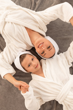 Mother And Daughter Wearing Bathrobes And Towels On Head Lying On Bed