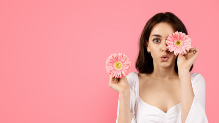 Shocked young caucasian female puts flower to eye, enjoys free time, has funの写真素材