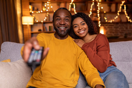 Portrait of loving black couple watching TV at homeの写真素材