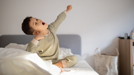 Cheerful active caucasian little child wake up, sits on bed, stretching body, yawns in bedroom interior, panoramaの写真素材