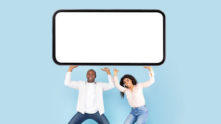 African american couple holding huge heavy smartphone with mockup on blank screen above their heads