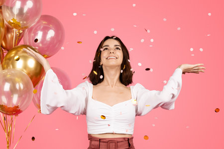 Satisfied inspired pretty young european lady with many balloons enjoying confetti, has funの写真素材