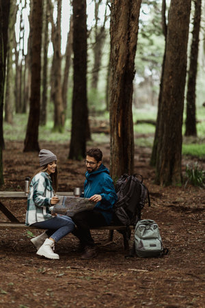 Glad young european man and lady tourists in jackets with backpack resting in forest, enjoy cold season outdoorsの写真素材