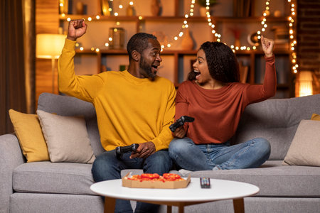 Cheerfy african man and woman holding joysticks, raising hands upの写真素材