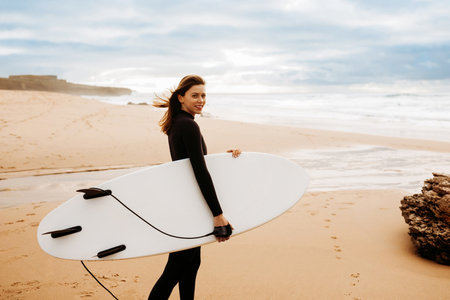 Extreme sports. Young woman in swimsuit walking on beach with surf board, looking and smiling at camera, copy spaceの写真素材