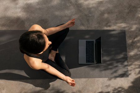 Caucasian millennial slim female in sportswear practicing yoga, meditates on mat, watch video lesson with coachの写真素材