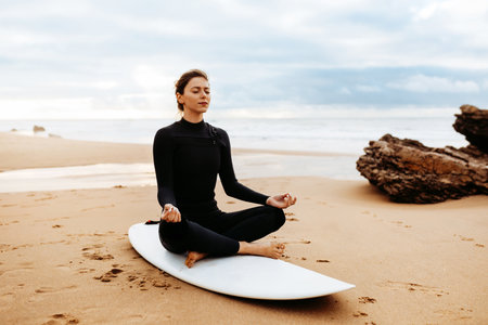 Yoga sup board. Fit european woman in swimsuit meditating on surf board on beach by seaside, free...