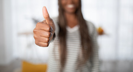 Unrecognizable black woman showing thumb up, home interiorの写真素材