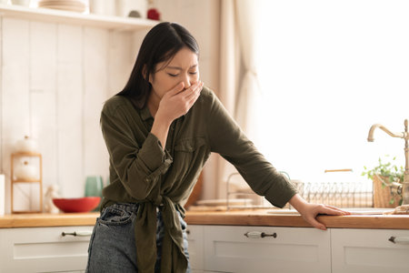 Young asian woman feeling nausea in kitchen, cover mouthの写真素材