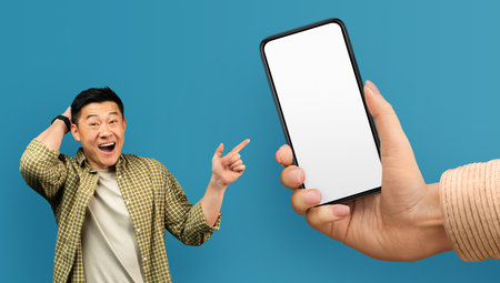 Cool Offer. Excited Asian Man Pointing At Blank Smartphone In Huge Hand