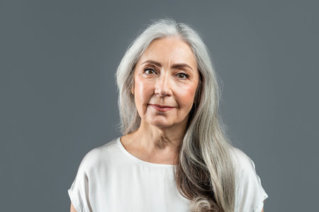 Smiling old european female with gray hair looking at camera, isolated on gray background, studio