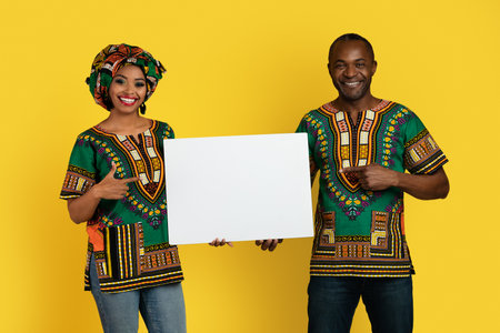Emotional black couple in traditional costumes showing blank placardの写真素材