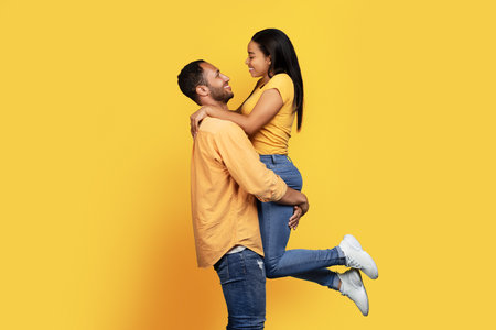 Happy young african american guy in casual raises woman on hands, have fun in free time, rejoice victoryの写真素材