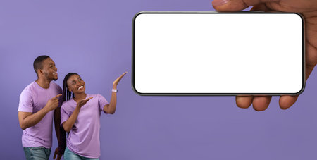Cheerful Black Couple Pointing At Huge Blank Cellphone In Big Female Handの写真素材