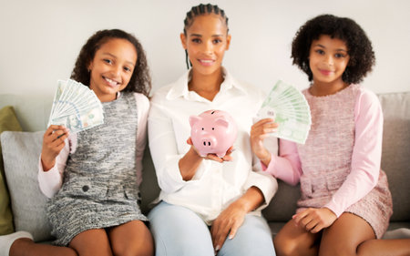 Black Mom And Daughters Holding Piggybank With Savings At Homeの写真素材