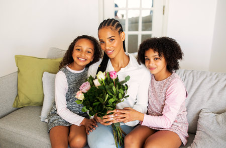 Cheerful Black Girls Hugging Mommy Giving Flowers Sitting At Homeの写真素材