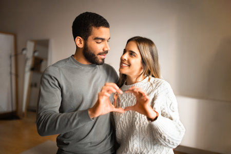 Smiling millennial european female and arab guy have fun, make heart sign with hands together, hold...