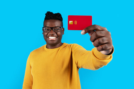 Smiling Black Man In Eyeglasses Showing Red Credit Card At Cameraの写真素材