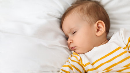 Beautiful baby girl sleeping peacefully on bed, resting during daytime sleep with eyes closed,...