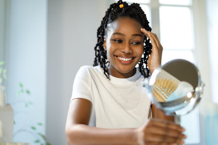Skin care and facelift concept. Happy black lady massaging her face sitting in front of mirror in...