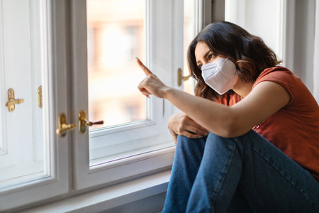 Quarantive Concept. Arab Female Wearing Protective Mask Sitting Near Windor At Homeの写真素材