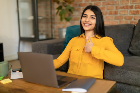 Positive mexican lady showing thumbs up gesture and using laptop computer, doing homework, recommending online schoolの写真素材