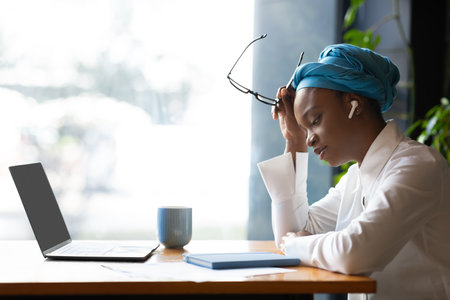 Exhausted black businesswoman working online, cafe interior, side viewの写真素材
