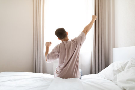 Rear view of man in pajamas stretching in bedの写真素材
