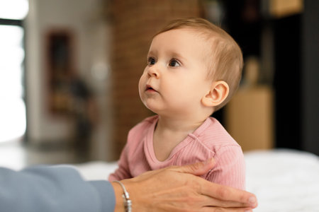Childcare concept. Cute little baby girl sitting on bed and looking at mom, relaxing together in...