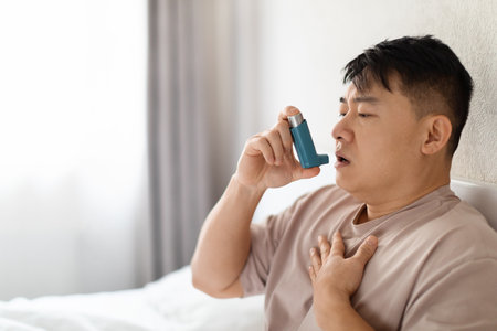 Asian man using inhaler sitting in bed at bedroomの写真素材